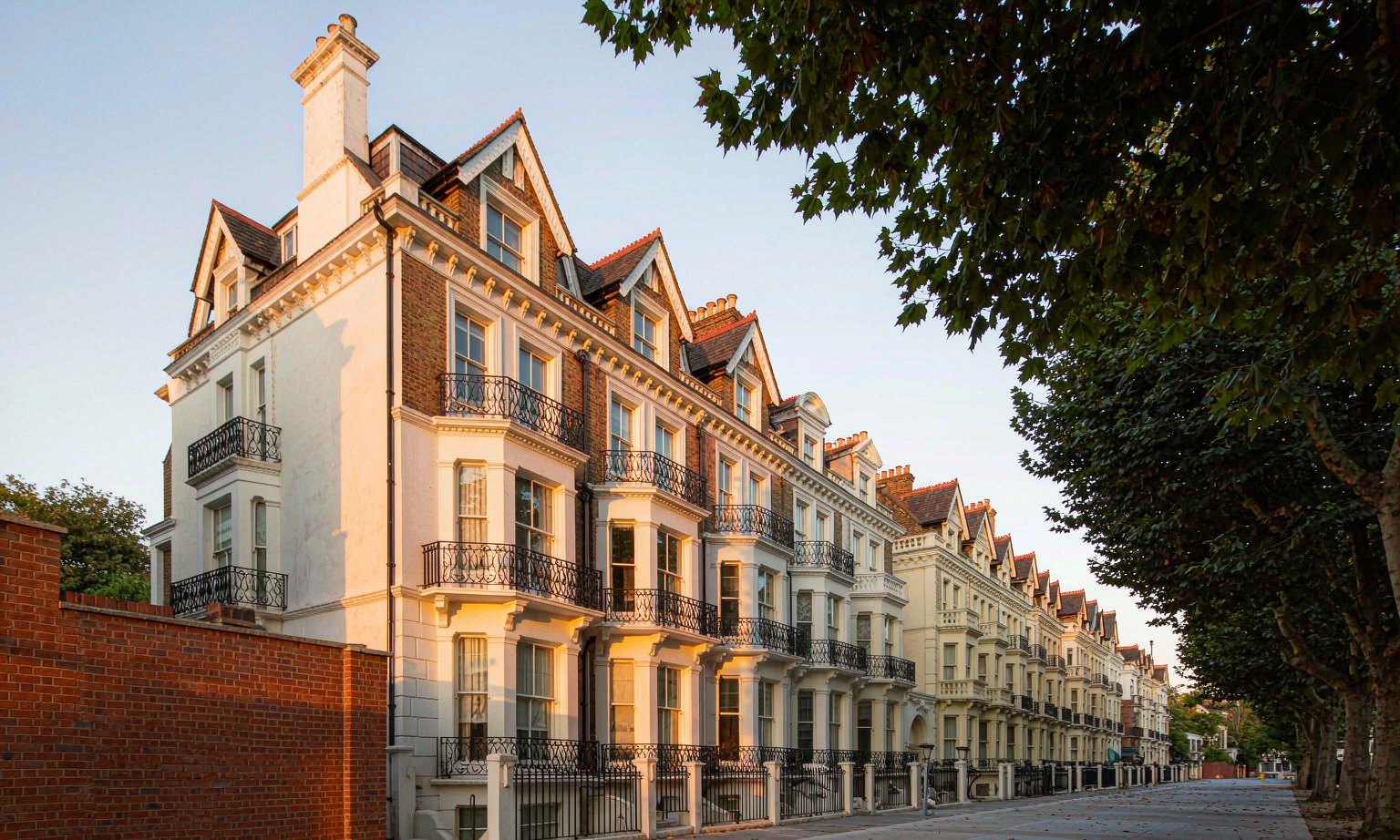 A row of white-stucco and brick Victorian townhouses on a quiet West London street in warm evening light